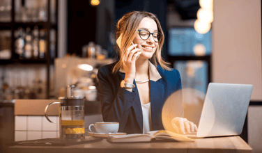 This is an image of a woman talking on the phone seated in front of an open laptop.