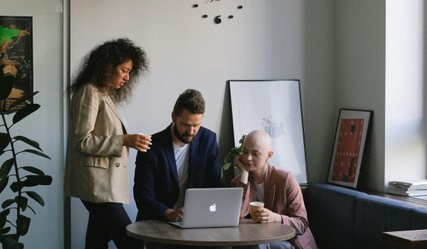 This is an image of three people gathered around a laptop in an office.
