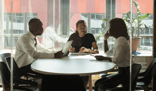 This is an image of three people sitting at a boardrrom table.