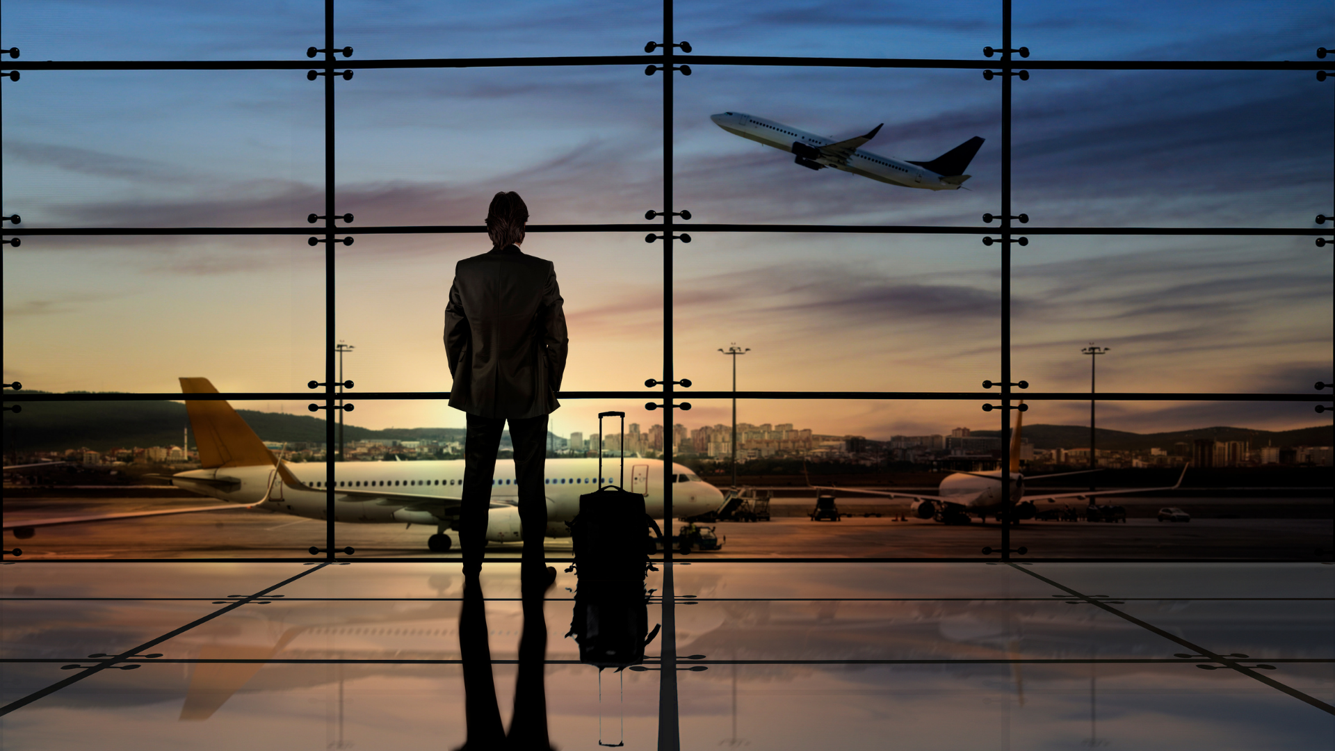 Business man standing in an airport looking out the window at a plane.