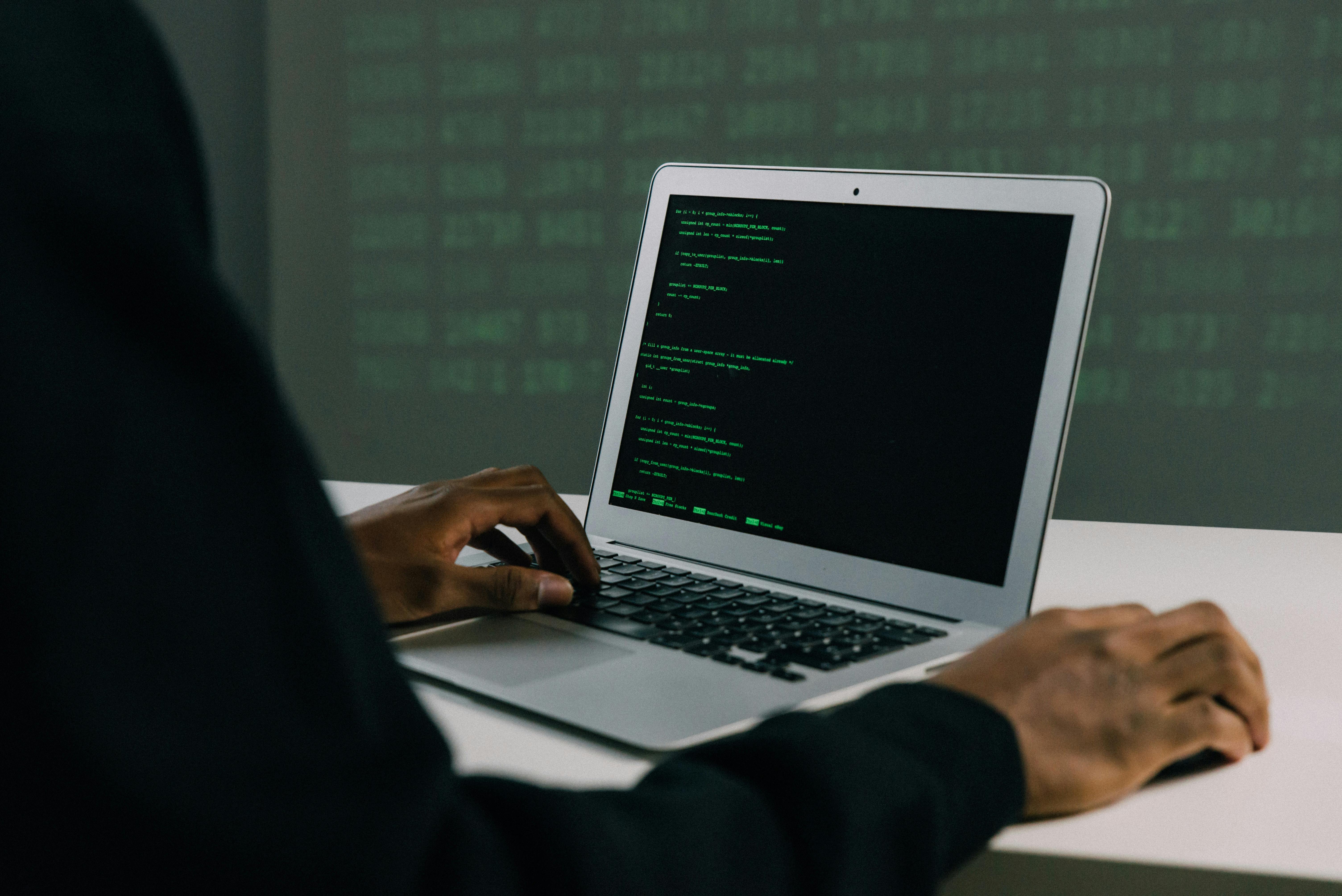 This is an image with a man sitting in front of a laptop with some code on it.
