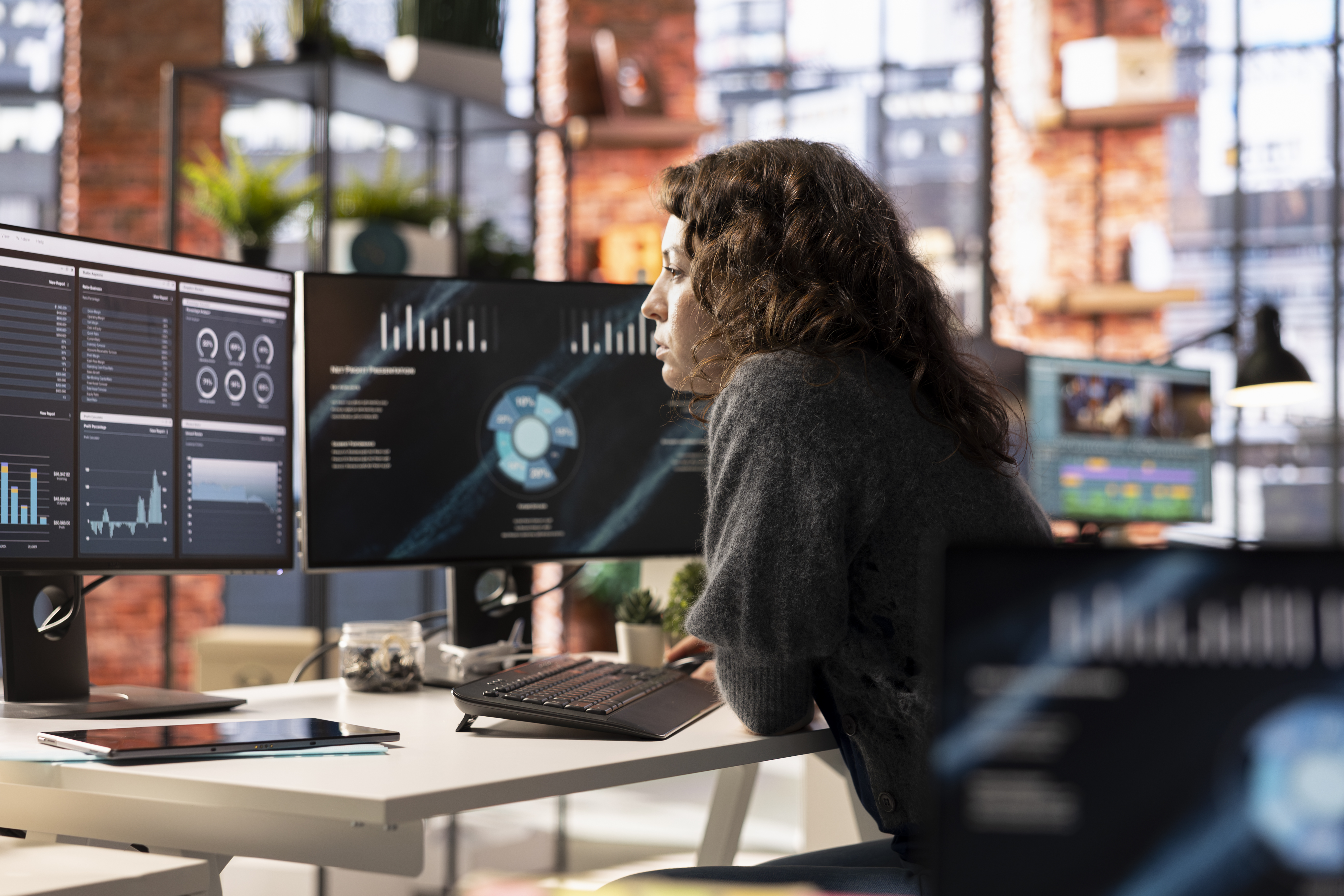This is an image of a woman working at a desk with two monitors in front of her.